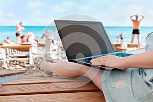 A person uses a laptop. In the background, the sea and the beach. The concept of freelancing and studying