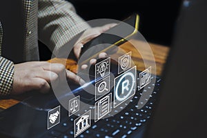 A person using a laptop and smartphone, with holographic icons floating above the keyboard, symbolizing intellectual property, photo