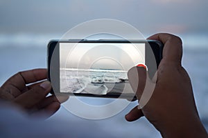 Person using phone. Person capturing beach landscape by cellphone in hand.