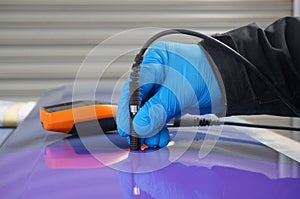 Person using probe, with digital tester, to measure the paint thickness microns on a painted metal panel.