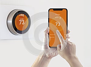 A person using a smart phone application warming up the room temperature with a wireless smart thermostat on a white background