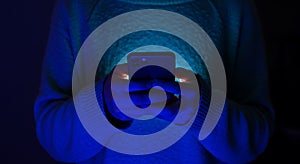 Person using smartphone in dark blue light for communication and entertainment