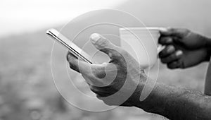 Person using smartphone. Hand of businessman checking phone while holding a cup of tea in black and white background