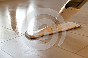 Person using spray mop pad and refillable bottle with cleaning solution, mopping the floor in apartment