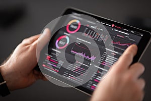 Person using tablet displaying colorful business analytics and data visualization charts on screen