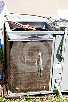 Person using water hose to clean condenser coil on air conditioner system