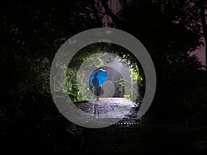 Person waiting with blue umbrella at night in the rain