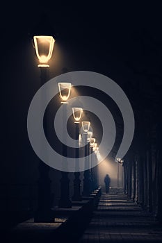 Person walking on dark street illuminated with streetlamps