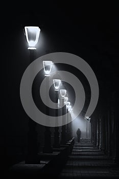 Person walking on dark street illuminated with streetlamps