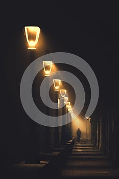 Person walking on dark street illuminated with streetlamps