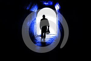 Person walking through tunnel towards light at end. Accomplishing goal or leaving darknenss for light