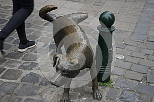 A person walks past a sculpture of a dog about to pee on a pole