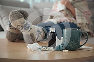 Person in warm socks near table with different remedies, closeup. Influenza virus