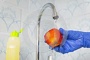 Person washes fruit with eco soap for washing in a kitchen with blue walls. Decontamination and disinfection of products