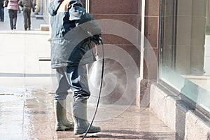 The person washes the sidewalk from a hose before show-window of shop