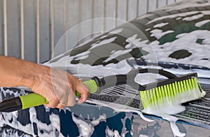 A person is washing a car with a green and black brush