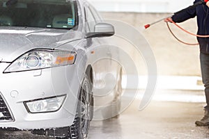 Person washing car with water and soap in carwash.