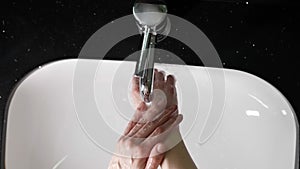 person is washing hands in bathroom, top view on hands under stream of water