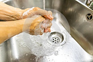 Person washing hands with soap in kitchen sink