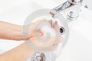 Person washing his hands hygienically with soap under the tap photo