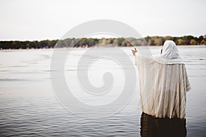 Person wearing a biblical robe standing in the water with a hand up