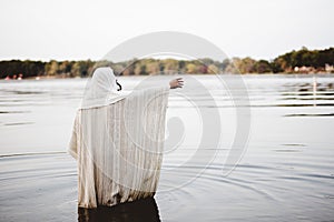Person wearing a biblical robe standing in the water with a hand up shot from behind