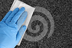 Person wearing gloves cleaning granite kitchen worktop counter with an anti-bacterial wipe cloth.