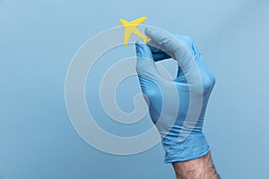 A person wearing a medical surgical glove holding a yellow travel airplane photo