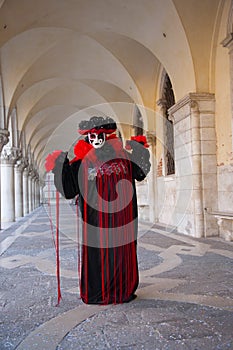 Person wearing a Venetian mask and a black and red costume under arches of Doges Palace at the Venice Carnival in Venice Italy
