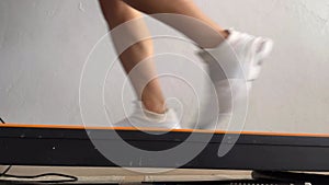 The person wearing white shoes is running on a treadmill, exercising at home.