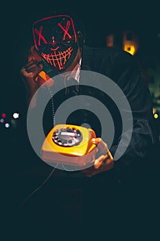 A person wears a lighted mask, Halloween, costume, purge mask with rotary phone