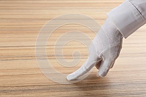 Person in white glove checking cleanliness of wooden  table, closeup. Space for text