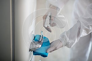 Person in white workwear and gloves disinfecting the fridge