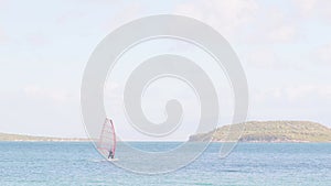 A person is windsurfing on the ocean with a red sail