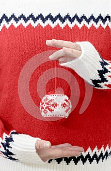 Person in winter sweater holding Christmas balls in hands.