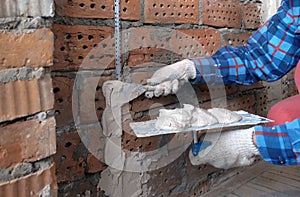 Person in work gloves  hand in the frame holds a trowel with plaster and attaches construction beacons to a brick wall with a sp