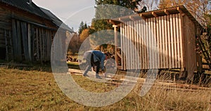 Person working on constructing a wooden structure outdoors near a log cabin. DIY home improvement and rustic living