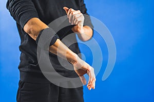 a person wrapping an elbow support brace to reduce pain, blue background injured hand