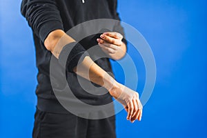 a person wrapping an elbow support brace to reduce pain, blue background injured hand