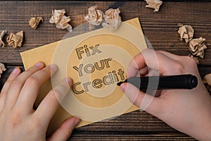 A person is writing on a piece of paper that says Fix Your Credit