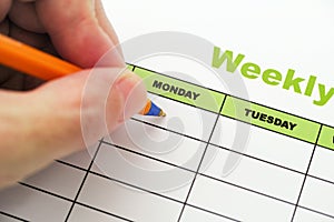 Person writing weekly schedule with ballpoint pen