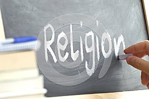 A person writing the word Religion on a blackboard.