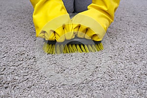 A person in yellow rubber glowes with a brush in hands cleaning carpet in house, cleaning home from dust