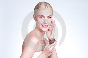Personable woman applying moisturizer cream on her face for perfect skin.