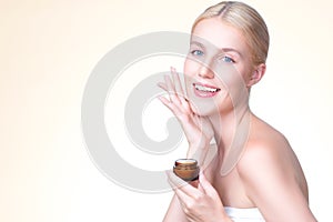 Personable woman applying moisturizer cream on her face for perfect skin.