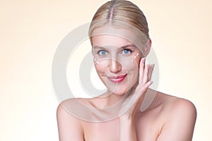 Personable woman applying moisturizer cream on her face for perfect skin