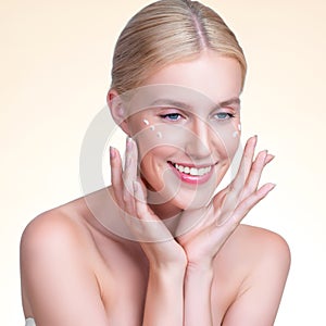 Personable woman applying moisturizer cream on her face for perfect skin