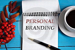 PERSONAL BRANDING - words in a white notebook on a wooden blue background with a rowan branch and a fragment of a cup of coffee