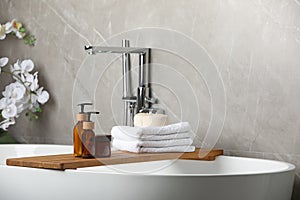 Personal care products and folded towels on bath tray indoors