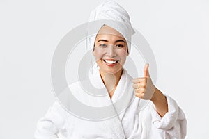 Personal care, women beauty, bath and shower concept. Satisfied happy asian girl in bathrobe and towel showing thumb-up